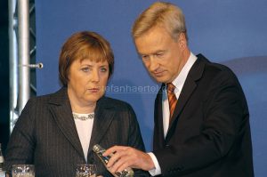 Zwei Personen vor blauem Hintergrund; Mann füllt Getränk aus Flasche in Glas.